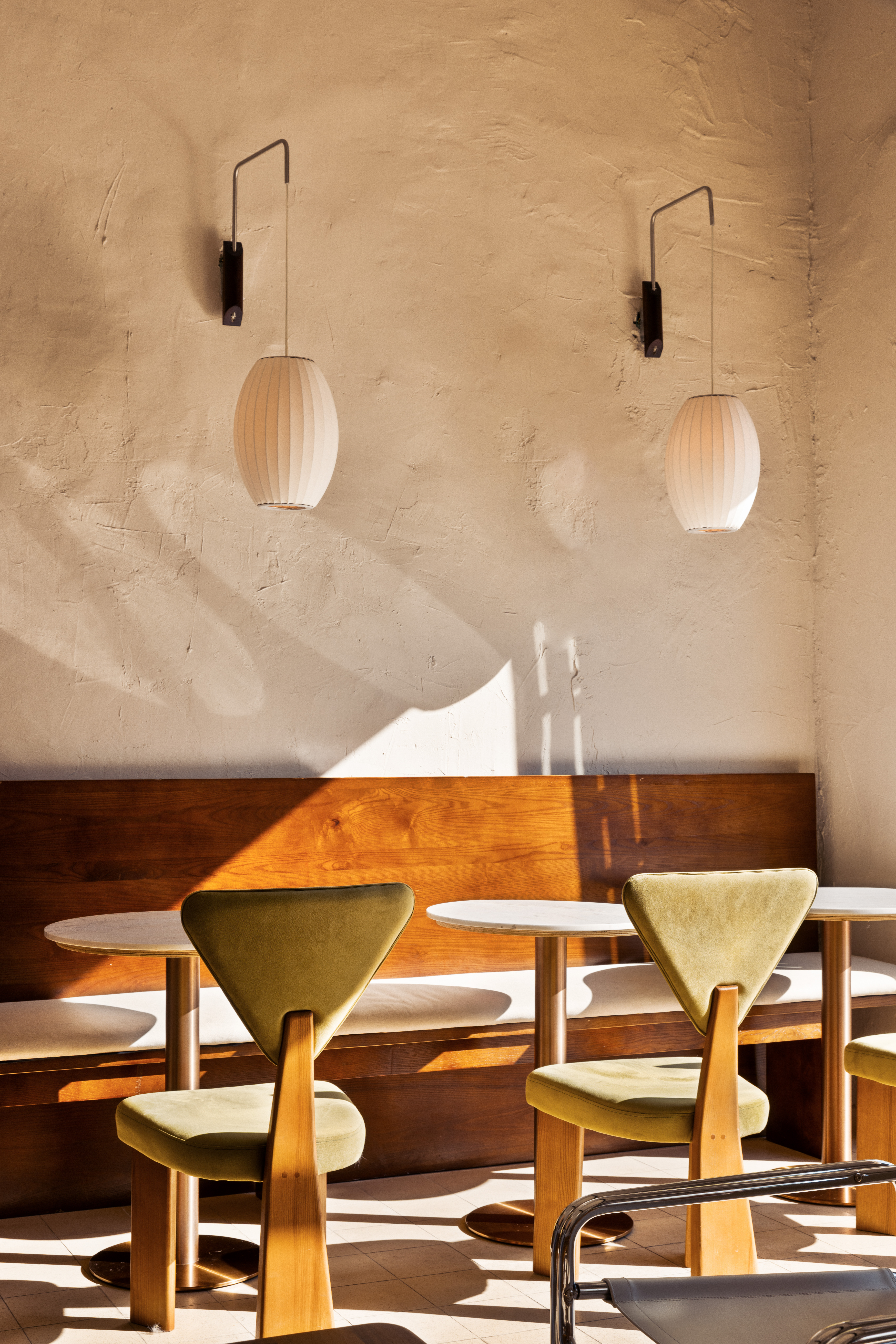 Sunlit cafe seating with green chairs, wooden benches and wall lamps.