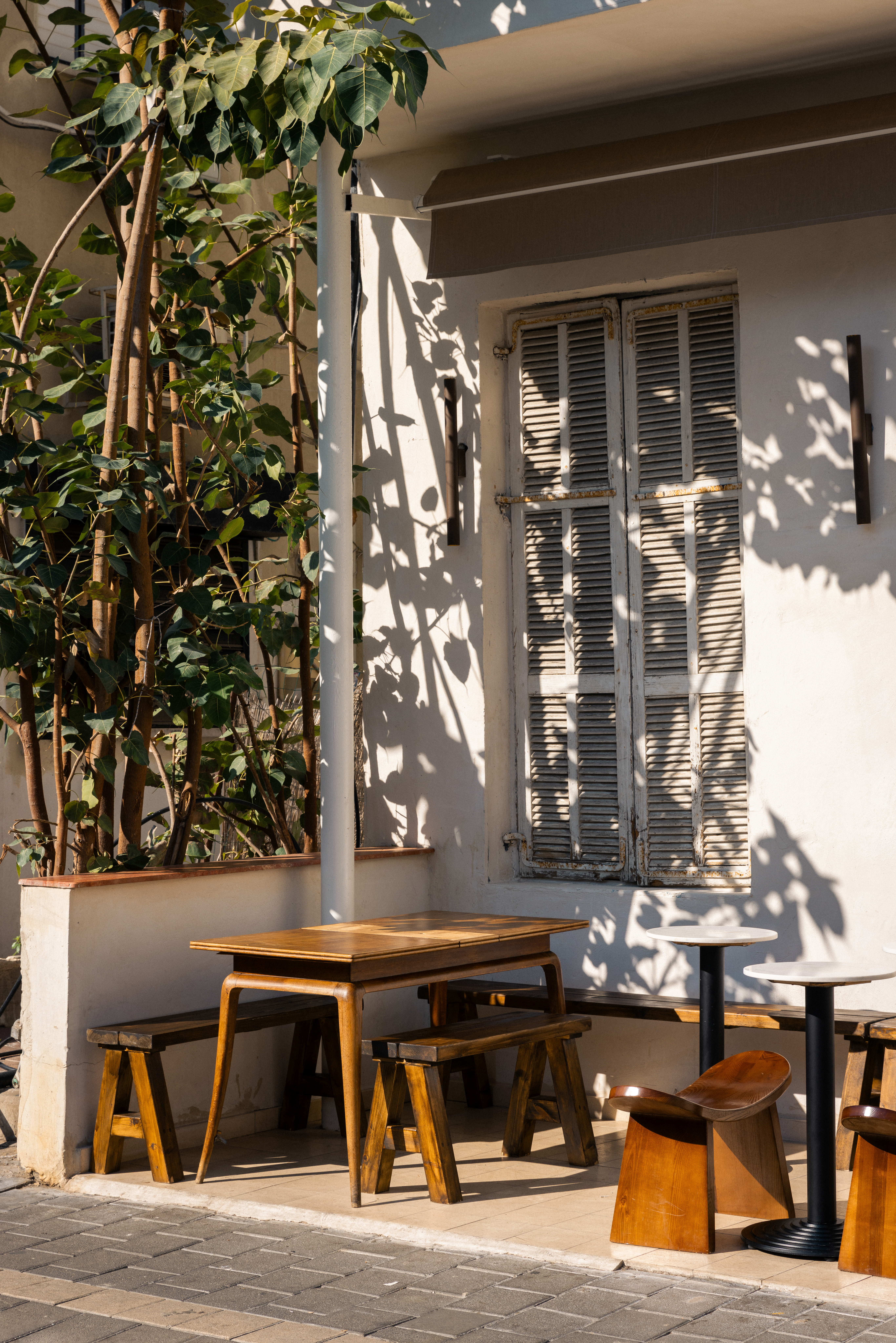 Outdoor cafe tables beside climbing plants and a window.