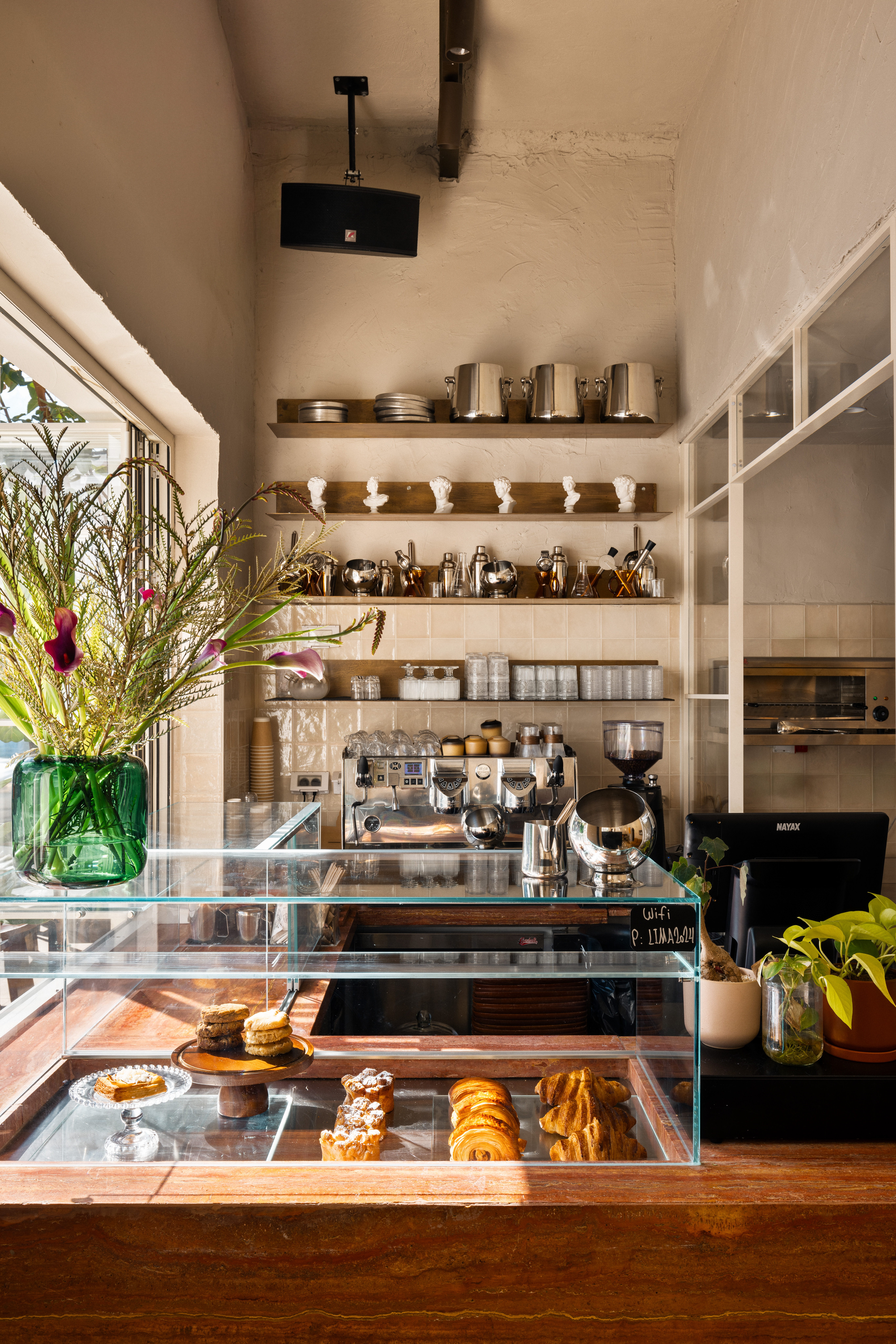 Lima Cafe counter with a pastry display, coffee machine and wall shelving.